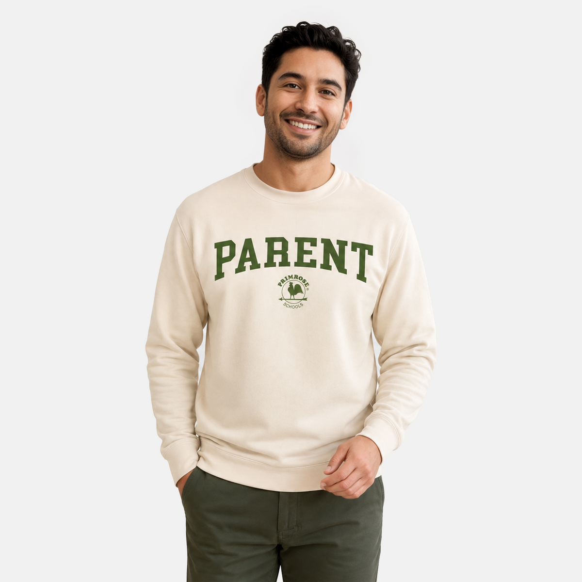 A man wearing a cream-colored crewneck sweatshirt with 'PARENT' printed in green varsity letters on the chest, paired with dark green pants, against a light gray studio background. -AI GENERATED IMAGE-